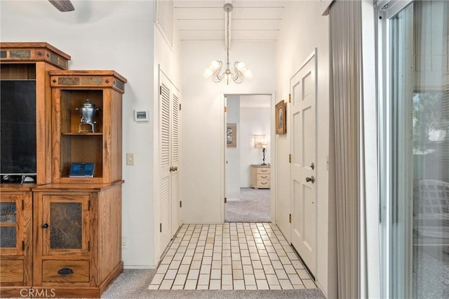 hallway with light colored carpet and an inviting chandelier