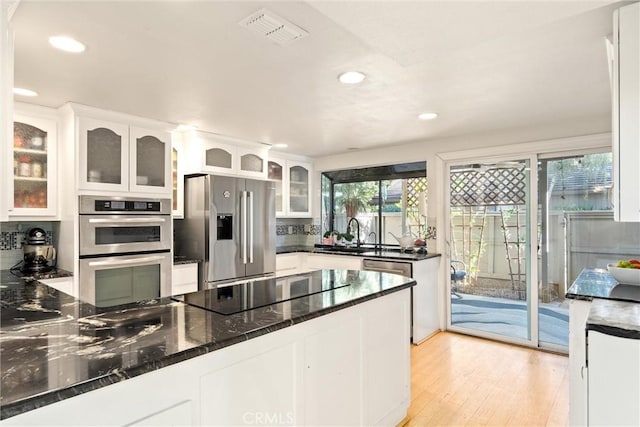 kitchen with dark stone counters, white cabinets, sink, light wood-type flooring, and stainless steel appliances