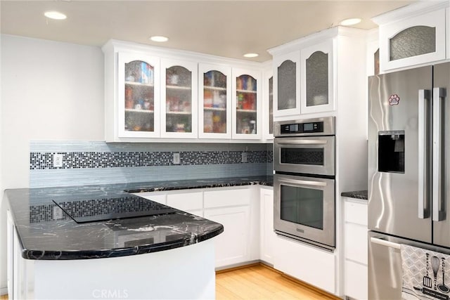 kitchen featuring stainless steel appliances, tasteful backsplash, dark stone counters, light hardwood / wood-style floors, and white cabinets