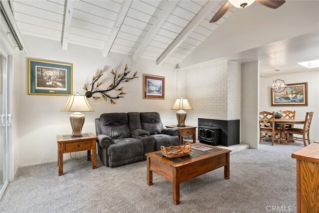 carpeted living room with vaulted ceiling with beams, a wood stove, ceiling fan with notable chandelier, and wooden ceiling