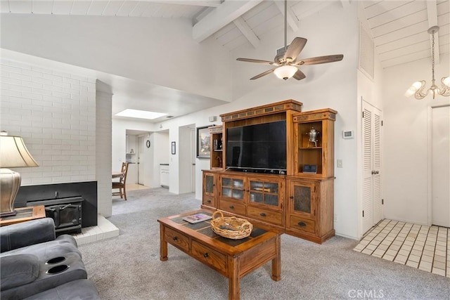 carpeted living room featuring ceiling fan with notable chandelier, beam ceiling, a wood stove, and high vaulted ceiling