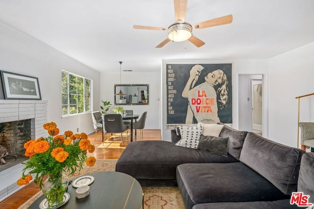 living room with ceiling fan, light hardwood / wood-style floors, crown molding, and a brick fireplace