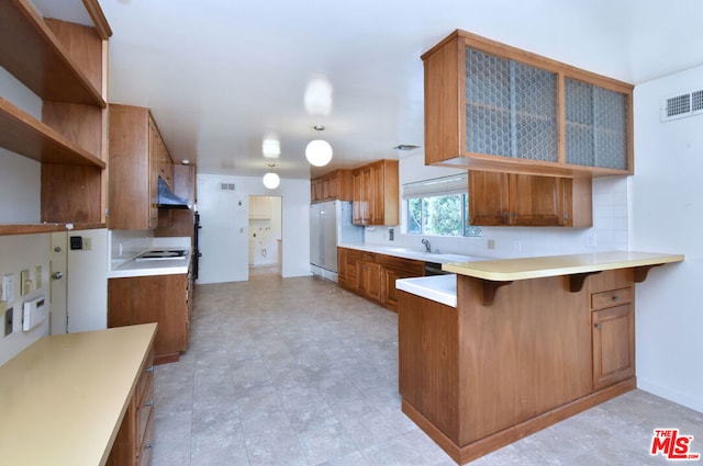 kitchen with a breakfast bar, white stovetop, sink, stainless steel fridge, and kitchen peninsula