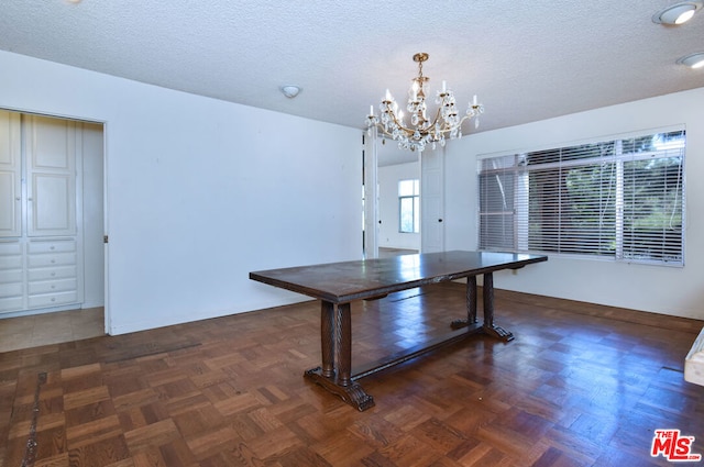 unfurnished dining area featuring dark parquet floors, a textured ceiling, and an inviting chandelier