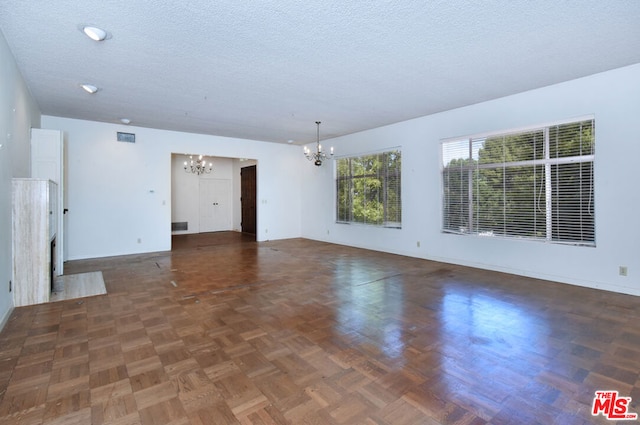 unfurnished living room with dark parquet flooring, a textured ceiling, and a chandelier