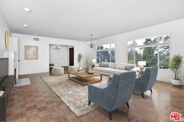 living room with a textured ceiling, an inviting chandelier, and parquet floors