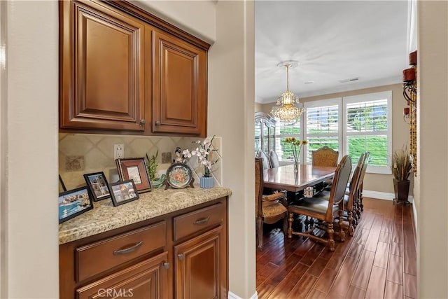 kitchen featuring light stone countertops, dark wood-type flooring, an inviting chandelier, tasteful backsplash, and pendant lighting