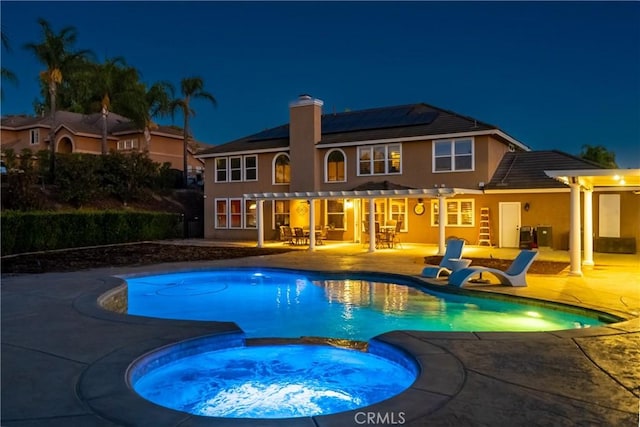 pool at night with an in ground hot tub and a patio area