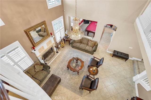 tiled living room with a notable chandelier, a towering ceiling, a fireplace, and a wealth of natural light