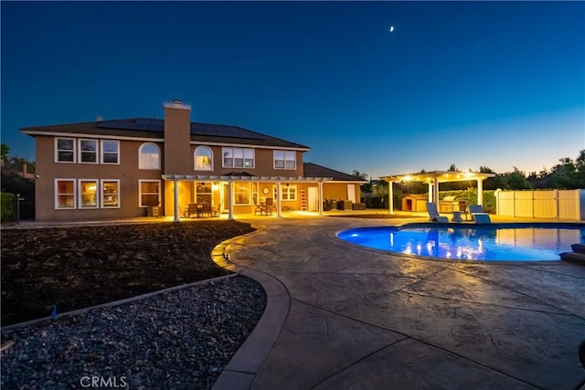 pool at dusk with a pergola and a patio area