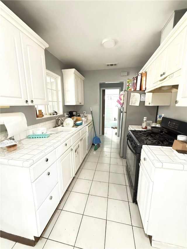 kitchen featuring tile counters, white cabinets, sink, and black gas range