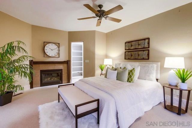 bedroom with ceiling fan, light colored carpet, and a tiled fireplace