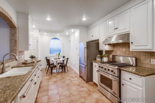 kitchen with backsplash, high end appliances, sink, stone countertops, and white cabinetry