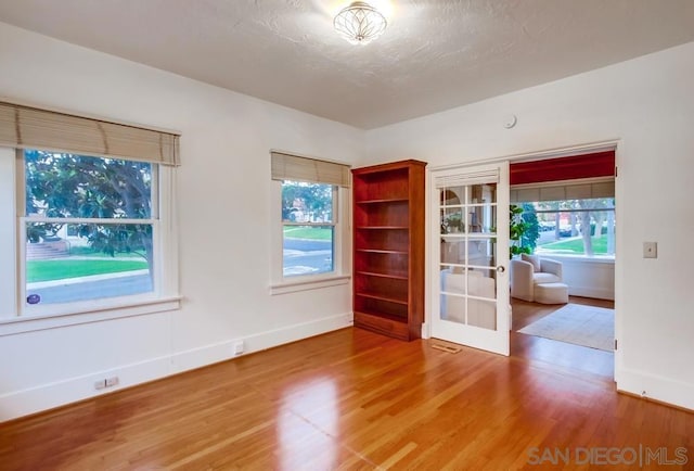 empty room featuring hardwood / wood-style flooring, a healthy amount of sunlight, a textured ceiling, and french doors