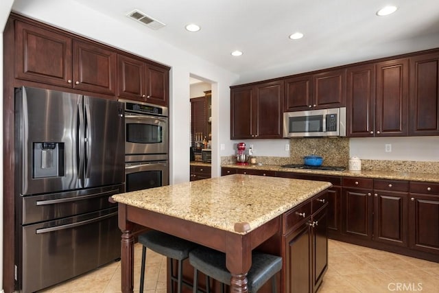 kitchen with light stone countertops, tasteful backsplash, stainless steel appliances, a kitchen island, and light tile patterned flooring