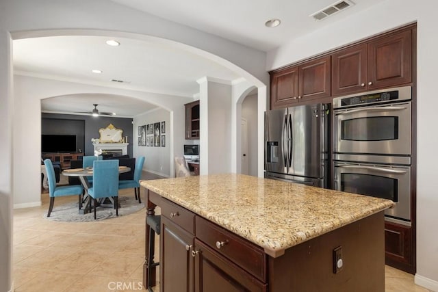 kitchen featuring ceiling fan, light tile patterned floors, appliances with stainless steel finishes, a kitchen island, and light stone counters