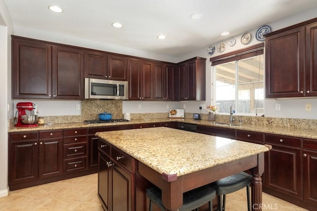 kitchen featuring sink, a center island, light stone counters, a breakfast bar, and appliances with stainless steel finishes