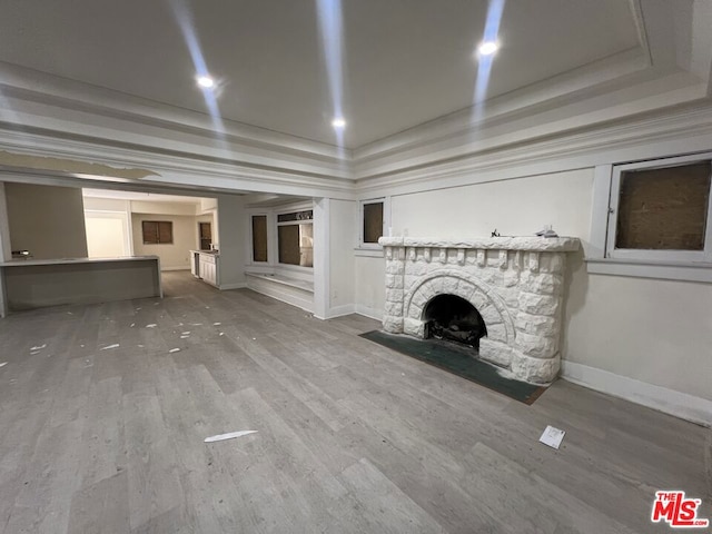 unfurnished living room featuring a tray ceiling, a fireplace, hardwood / wood-style floors, and ornamental molding