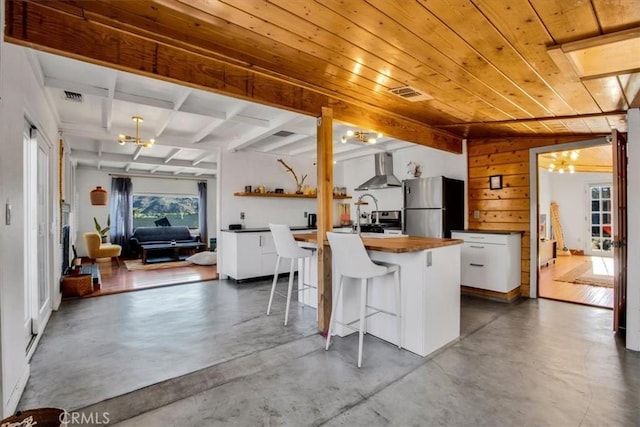 kitchen with a kitchen breakfast bar, wall chimney exhaust hood, white cabinetry, stainless steel refrigerator, and an island with sink