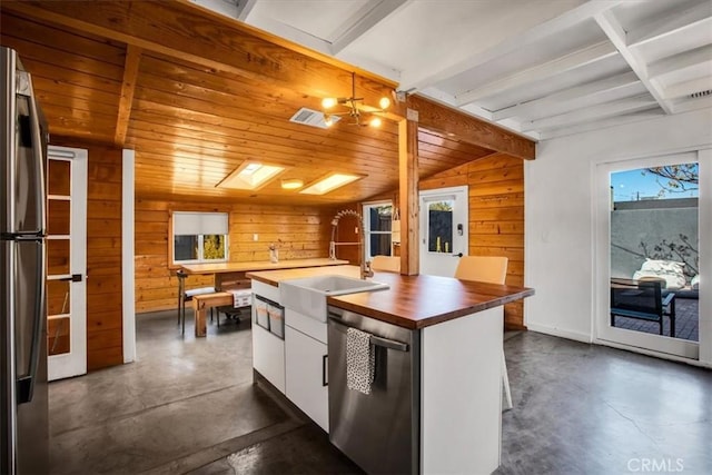 kitchen with butcher block counters, white cabinetry, sink, stainless steel appliances, and vaulted ceiling