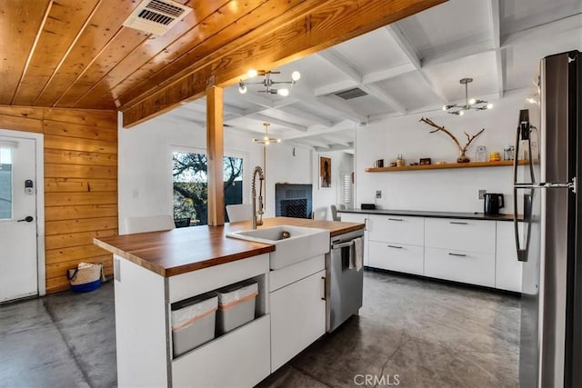 kitchen featuring stainless steel appliances, sink, lofted ceiling with beams, a center island with sink, and white cabinetry