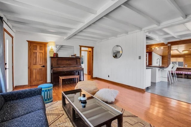 living room featuring wood walls, sink, beamed ceiling, and light wood-type flooring