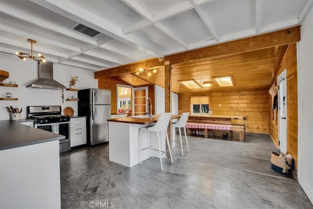 kitchen featuring a kitchen bar, stainless steel appliances, wooden walls, sink, and wall chimney range hood