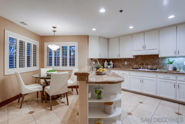 kitchen with decorative light fixtures, tasteful backsplash, white cabinets, light stone counters, and kitchen peninsula