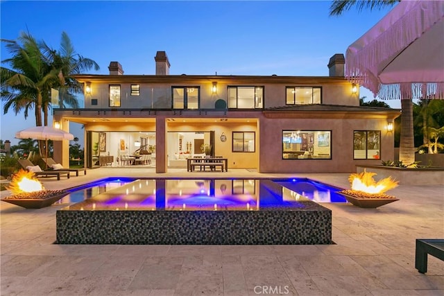 back house at dusk with a swimming pool with hot tub, an outdoor fire pit, and a patio area