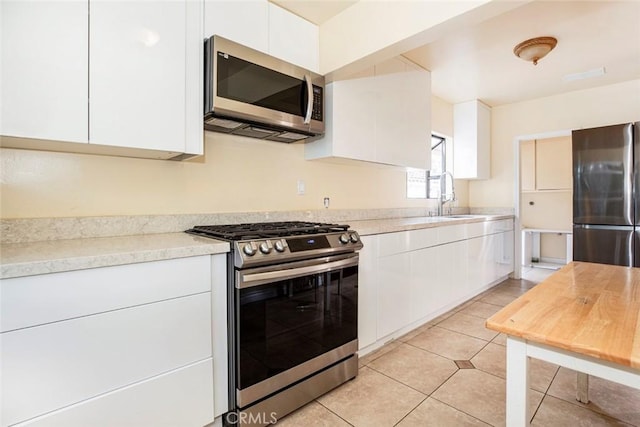 kitchen with white cabinets, sink, light tile patterned floors, and stainless steel appliances