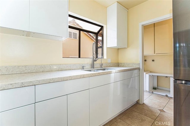 kitchen featuring white cabinets, light tile patterned floors, sink, and stainless steel refrigerator