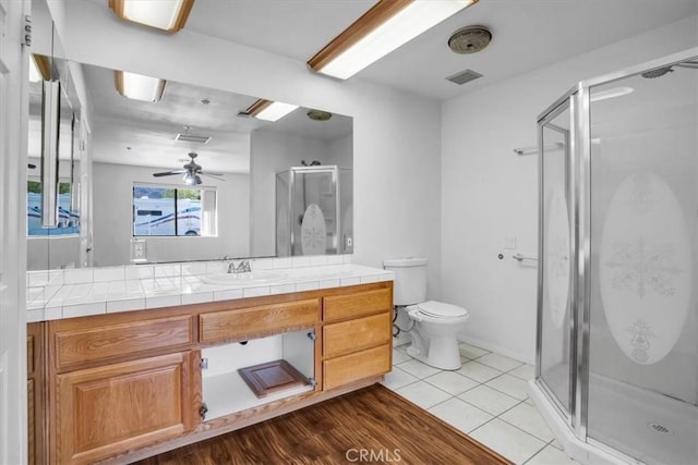 bathroom featuring ceiling fan, wood-type flooring, toilet, a shower with door, and vanity