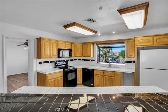 kitchen with tile counters, sink, tasteful backsplash, black appliances, and hardwood / wood-style flooring