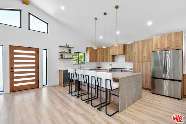 kitchen featuring a kitchen bar, light hardwood / wood-style flooring, hanging light fixtures, built in fridge, and an island with sink