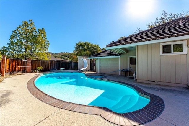 view of swimming pool featuring a hot tub, a water slide, a diving board, and a patio area