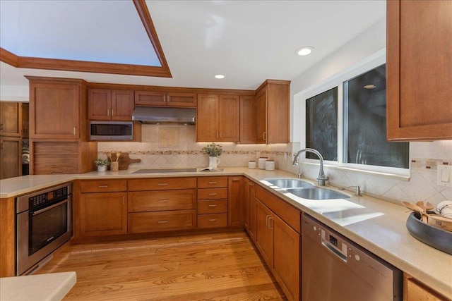 kitchen with tasteful backsplash, appliances with stainless steel finishes, sink, and light hardwood / wood-style floors