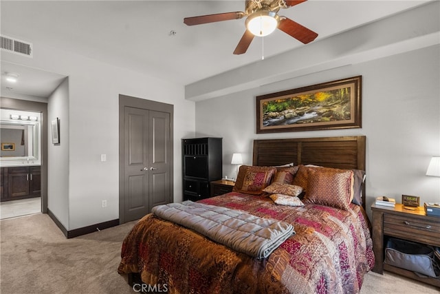 bedroom featuring a closet, ensuite bathroom, light colored carpet, and ceiling fan