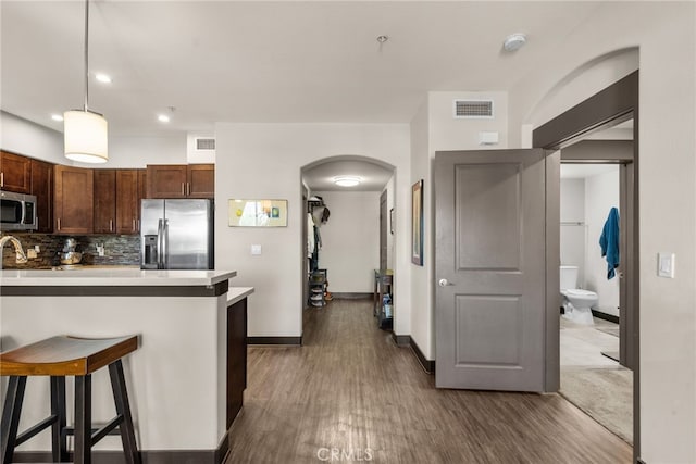 kitchen featuring a kitchen bar, appliances with stainless steel finishes, tasteful backsplash, dark hardwood / wood-style flooring, and hanging light fixtures