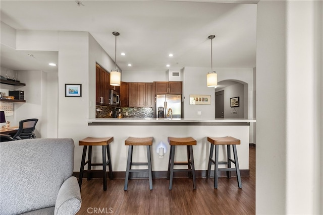 kitchen with kitchen peninsula, stainless steel appliances, backsplash, dark hardwood / wood-style flooring, and pendant lighting