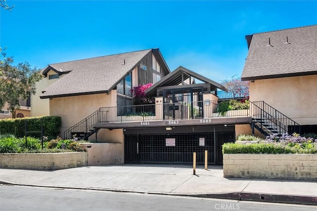 rear view of property featuring stairs, concrete driveway, and stucco siding