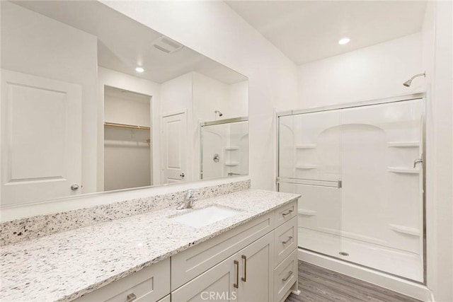 full bath featuring a walk in closet, recessed lighting, a stall shower, vanity, and wood finished floors