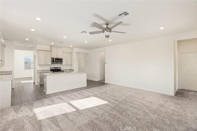 kitchen with visible vents, an island with sink, appliances with stainless steel finishes, open floor plan, and white cabinetry