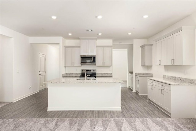 kitchen with a center island with sink, visible vents, light stone counters, stainless steel appliances, and white cabinetry