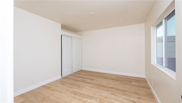 unfurnished bedroom with a closet, light wood finished floors, and baseboards