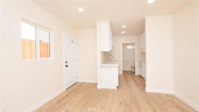 corridor with recessed lighting, a sink, light wood finished floors, and baseboards