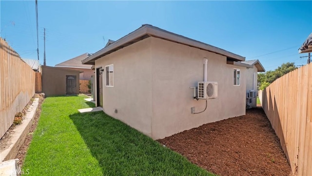 view of side of home with a lawn, a fenced backyard, an outbuilding, ac unit, and stucco siding