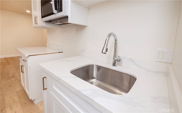 room details featuring light wood finished floors, light stone counters, white cabinets, and a sink