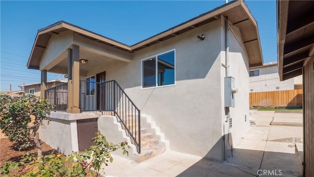 view of exterior entry with stucco siding, fence, and a patio