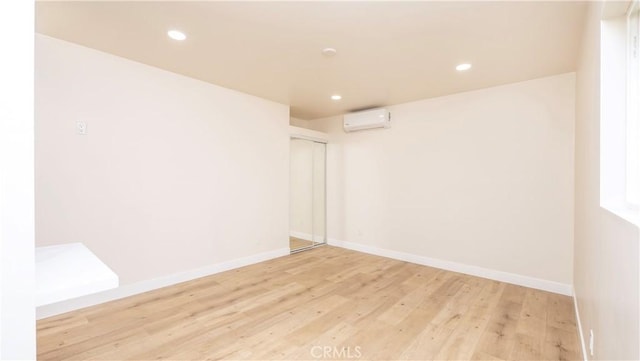 empty room with light wood-type flooring, an AC wall unit, baseboards, and recessed lighting