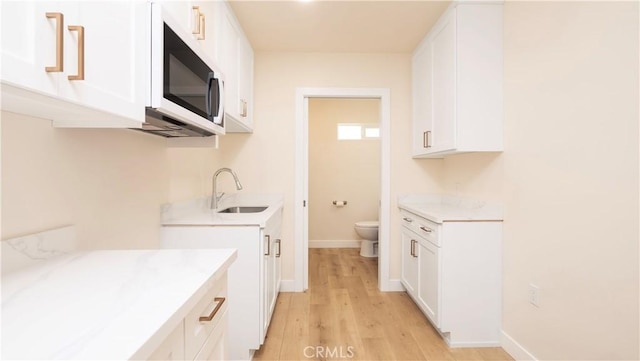 kitchen featuring white cabinets, white microwave, light countertops, and a sink